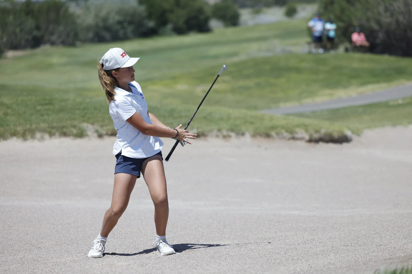 A junior golfer plays out of a greenside bunker.