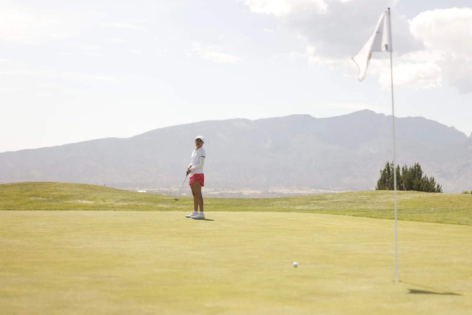 A junior golfer putts with mountains behind the green.